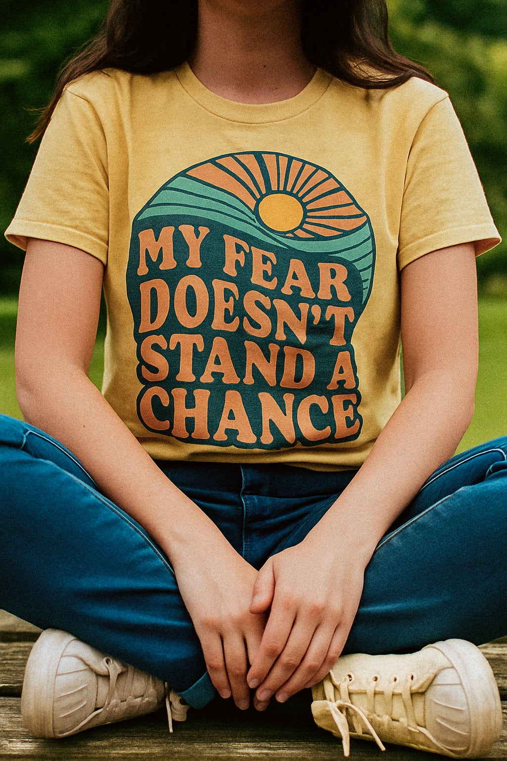 Yellow T-shirt with retro-style text and design. The front reads “MY FEAR DOESN’T STAND A CHANCE” in bold, vintage lettering over a graphic of a rising sun and waves in green, blue, and orange tones