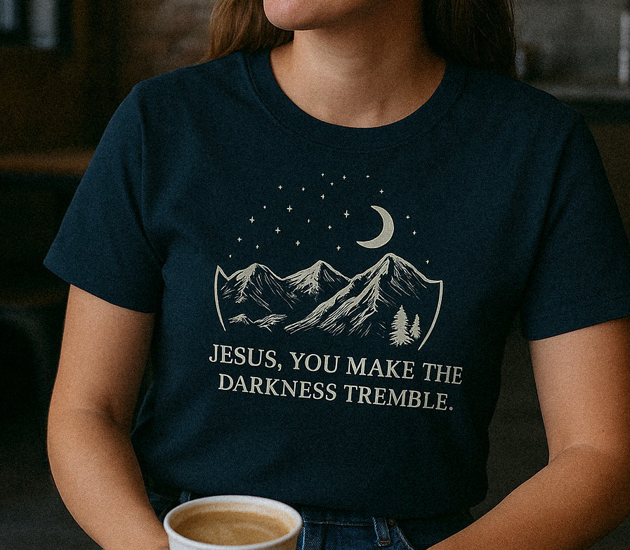 Young woman sitting at a wooden table in an industrial-style coffee shop, wearing a navy blue T-shirt that says