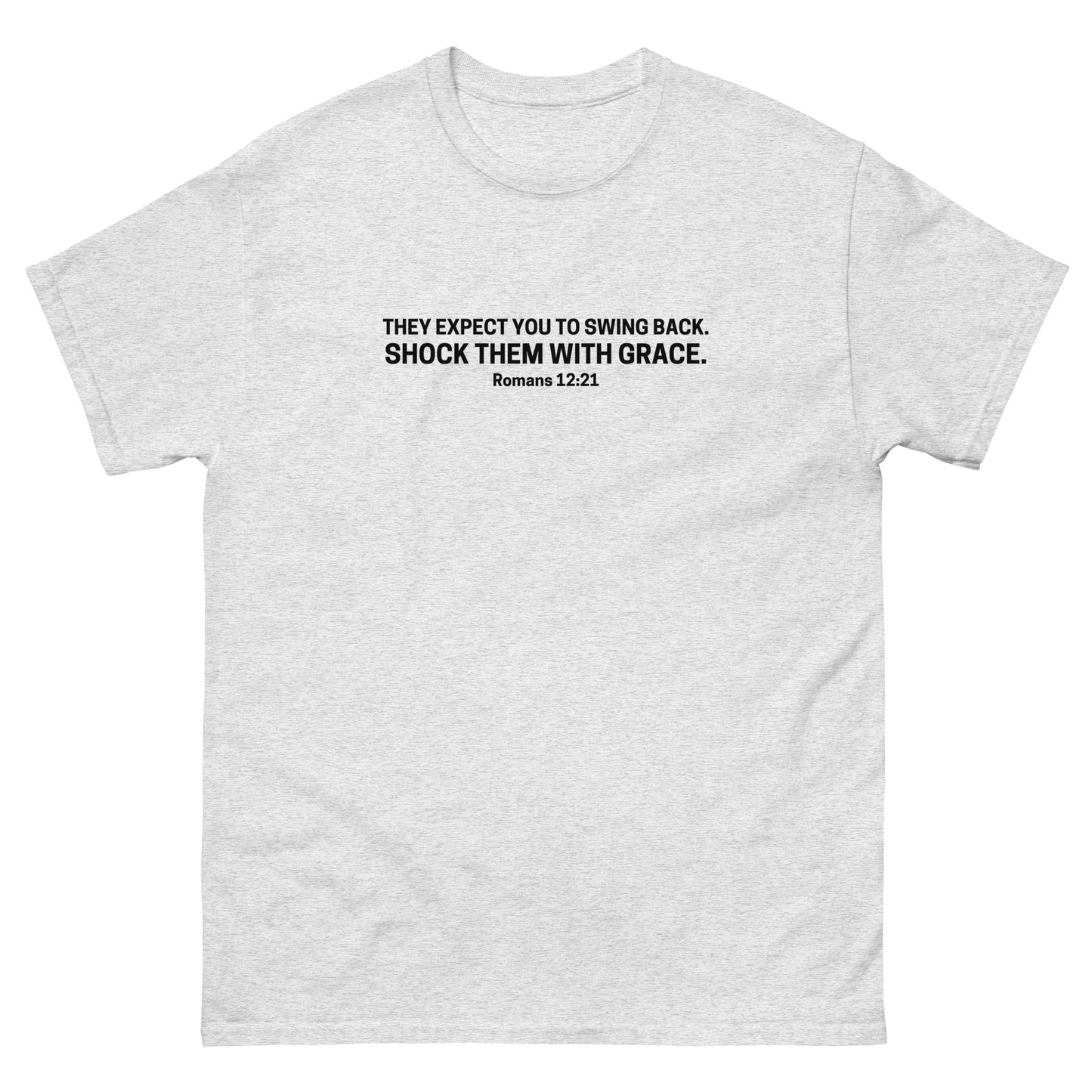 ash color t-shirt with black text on the front that reads 'They expect you to swing back. Shock them with grace. Romans 12:21,' displayed flat on a white background.