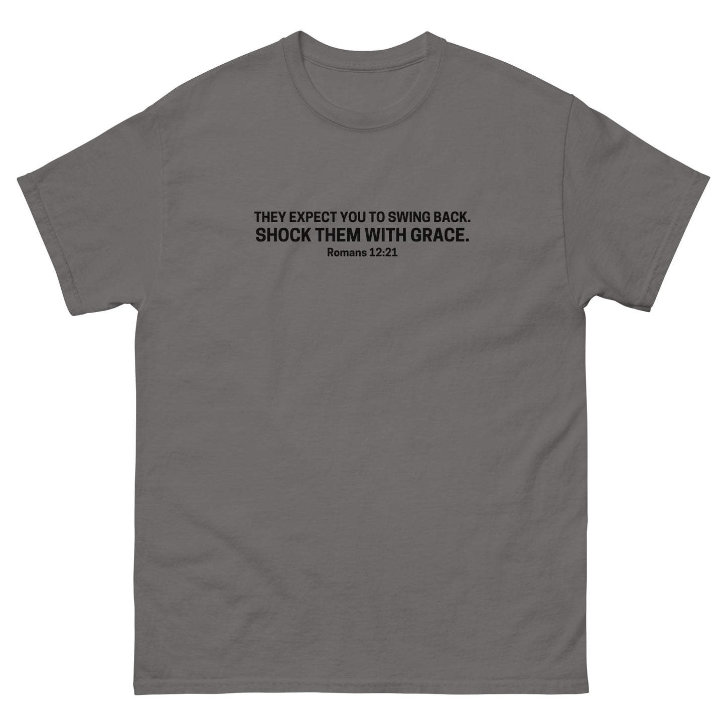  t-shirt with black text on the front that reads 'They expect you to swing back. Shock them with grace. Romans 12:21,' displayed flat on a white background. charcoal