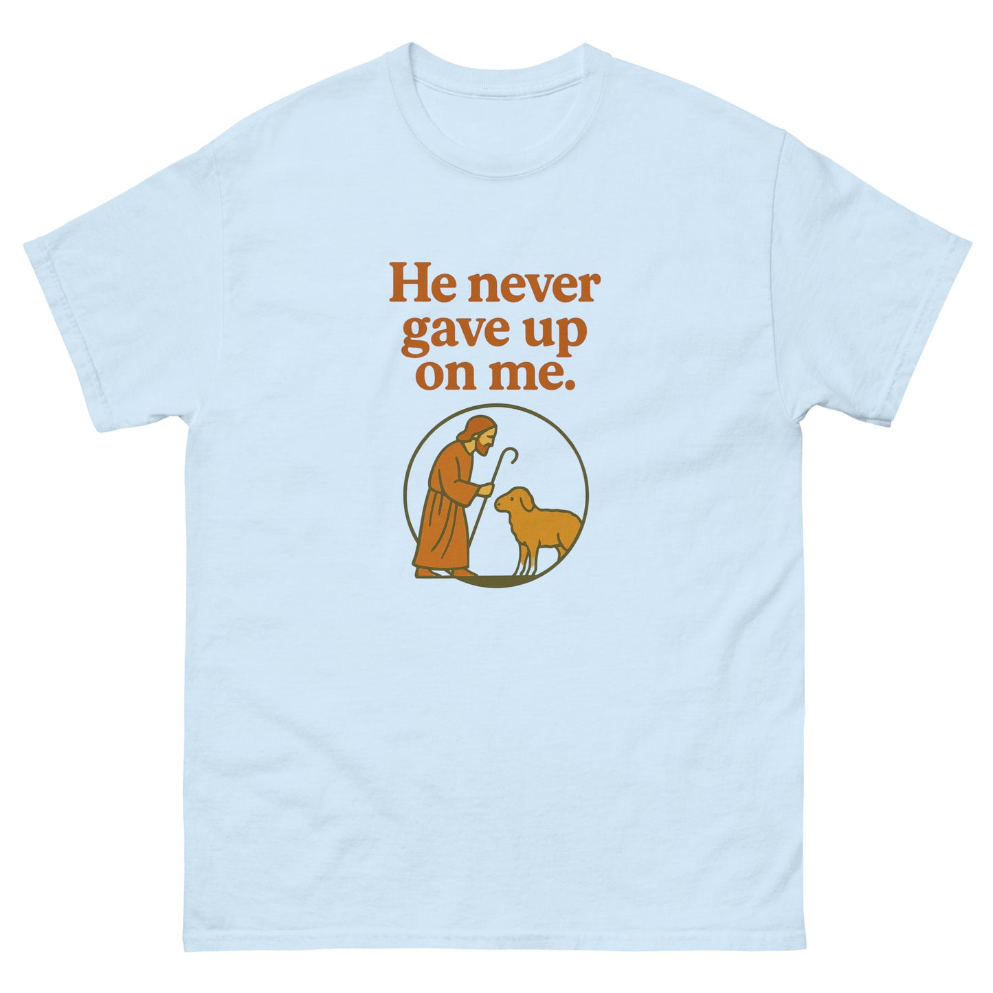 Christian T-shirt with the phrase 'He never gave up on me' above an illustration of Jesus as the shepherd standing with a sheep inside a circular frame. Front, Light Blue