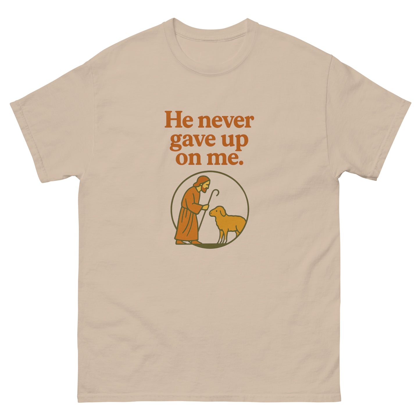 Christian T-shirt with the phrase 'He never gave up on me' above an illustration of Jesus as the shepherd standing with a sheep inside a circular frame. front, sand color