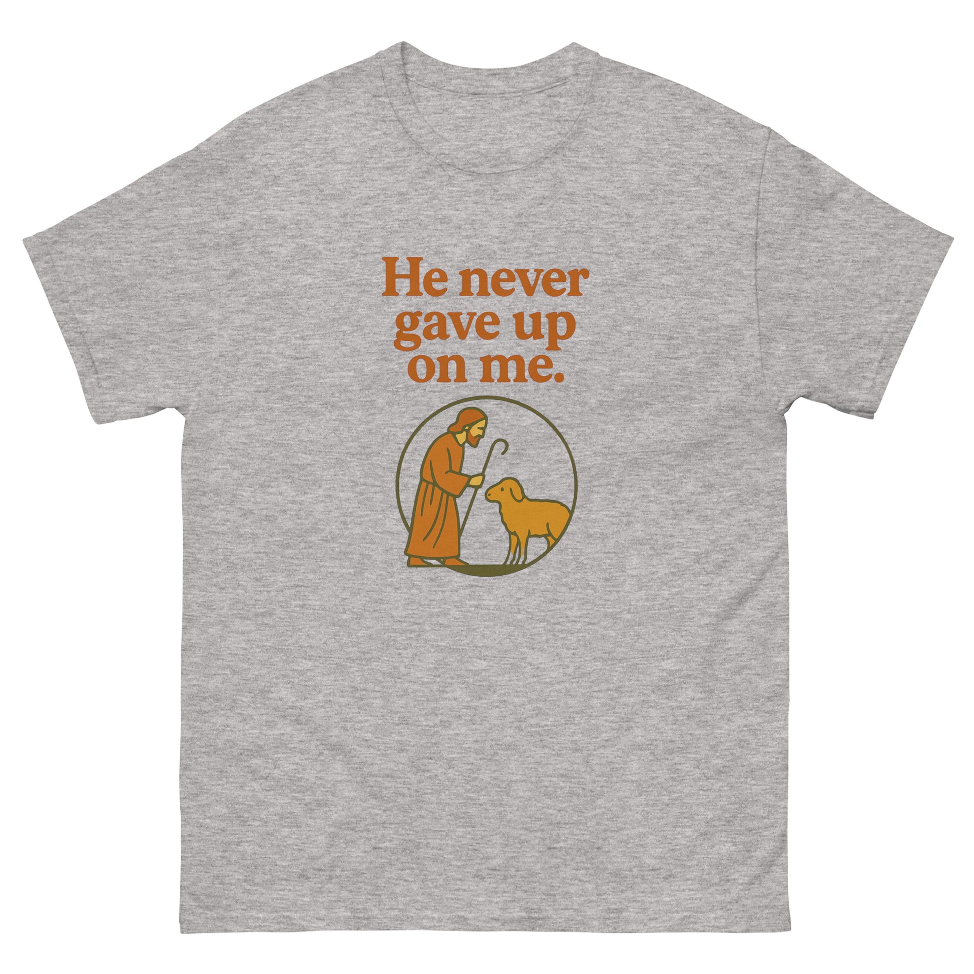 Christian T-shirt with the phrase 'He never gave up on me' above an illustration of Jesus as the shepherd standing with a sheep inside a circular frame. front, gray