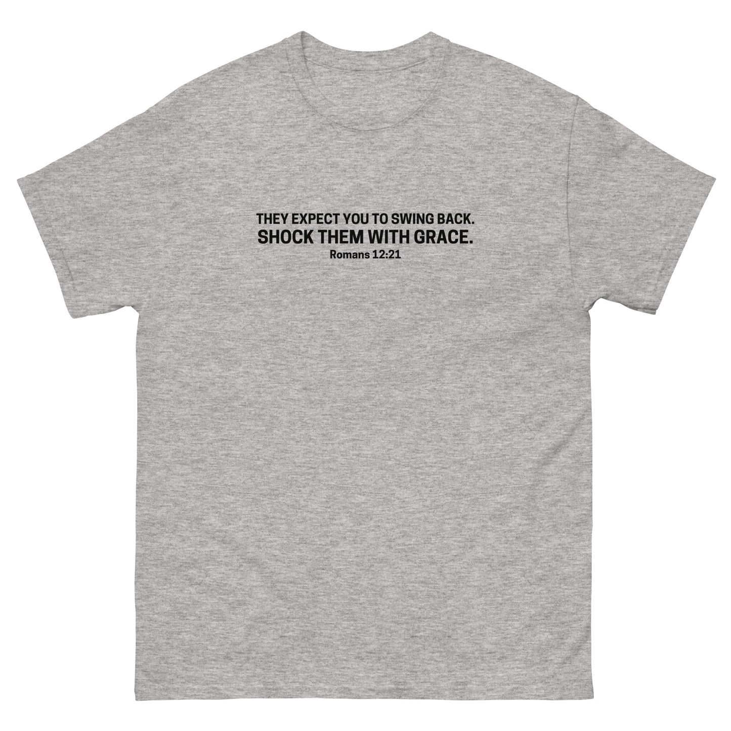 gray t-shirt with black text on the front that reads 'They expect you to swing back. Shock them with grace. Romans 12:21,' displayed flat on a white background.